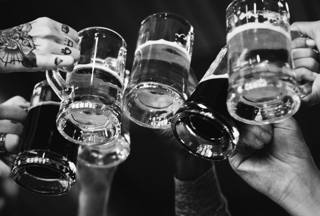 C'est une photo en noir et blanc de mains trinquant avec des chopes de bières remplies.